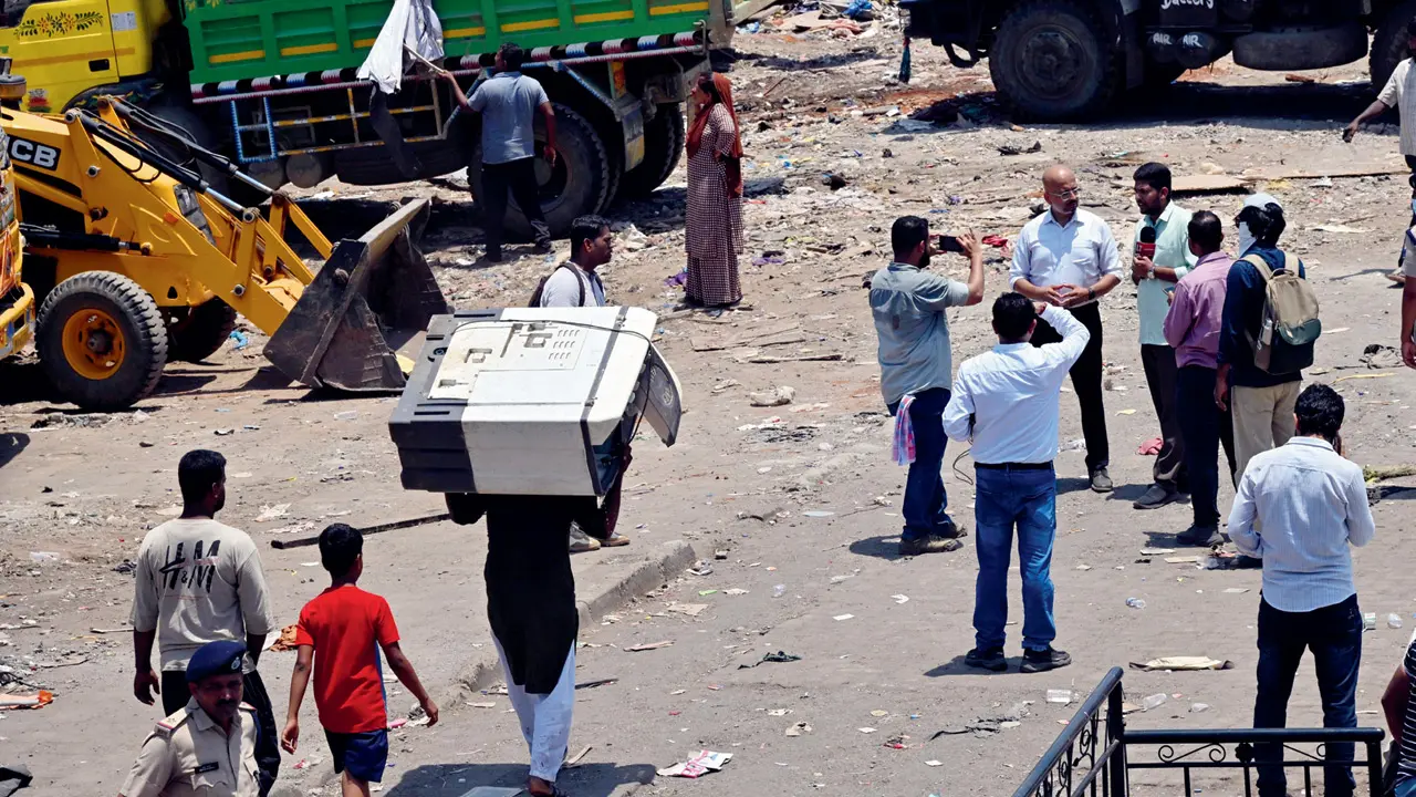 A resident carries a washing machine while vacating structures during the demolition drive at Garib Nagar in Bandra East
