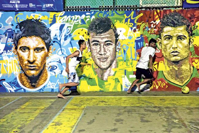 Youngsters play football in front of a mural of Argentina