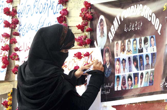 A mourner writes a message on a placard outside the army-run school in Peshawar where 149 people were massacred by the Taliban. Pic/AFP