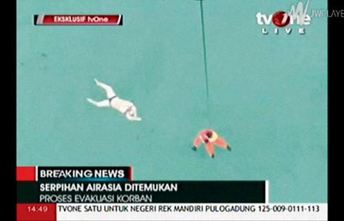 In this image taken from a video released by TV One, a rescuer is lowered on rope from a hovering helicopter near a bloated body in Java Sea waters 