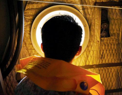 A serviceman of the Republic of Singapore Air Force (RSAF) onboard a C-130 aircraft looks out of a window during the search and locate (SAL) operation over the Java sea. 
