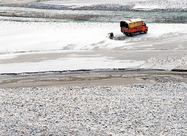 People load a truck with sand from a river bed in the high Himalaya mountains