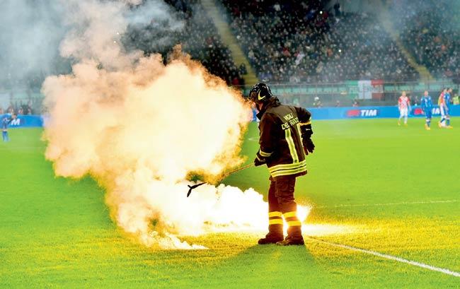 Flame and shame: A firefighter tries to douse the flares thrown onto the San Siro pitch by Croatian fans during Euro 2016 qualifier between Italy and Croatia in Milan on Sunday night. Pics/AFP