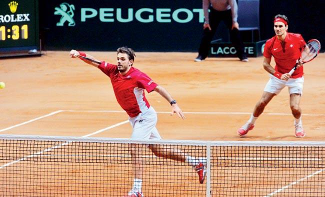 Reds hot: Switzerland-s Stanislas Wawrinka left returns while teammate Roger Federer looks in the doubles rubber of their Davis Cup final against France at the Stade Pierre Mauroy in Villeneuve-d’Ascq, northern France on Saturday. Federer-Wawrinka won 6-3, 7-5, 6-4. Pic/AFP