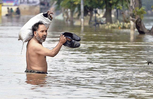 A man carries minimum essentials as he wades through a flooded street in Srinagar. Pic/PTI