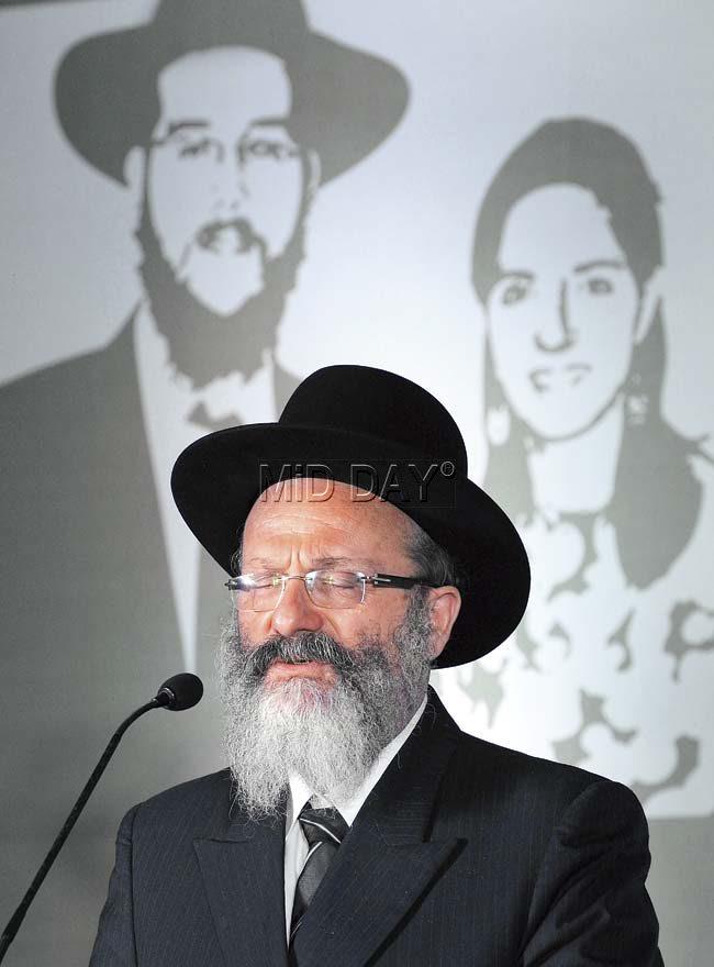Rabbi Nachman Holtzberg, father of the slain rabbi, speaks in front of an image of his son and daughter-in-law Rivka