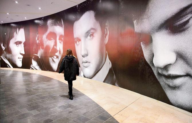 A woman poses next to large scale photographic prints of US singer Elvis Presley, during a photocall for the Elvis at the O2 exhibition in London on December 11, 2014. The exhibition will continue till August 31, 2015 and includes a variety of items from the Elvis archive, including costumes, cars, records and personal items such as Presley’s credit cards and house keys. PIC/AFP