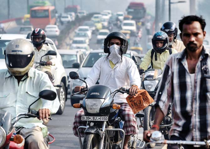 A biker uses a handkerchief to keep from breathing in the smoke in the air during rush hour in Delhi. Pic/AFP