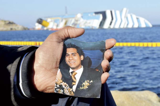 A file photograph shows Kevin holding out his brother Russel Rebello’s photo with the wreckage of Costa Concordia in the background. Pic/Getty Images
