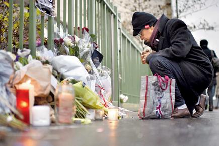 A passer-by prays in front of candles and flowers placed near the Charlie Hebdo office in memory of the deceased