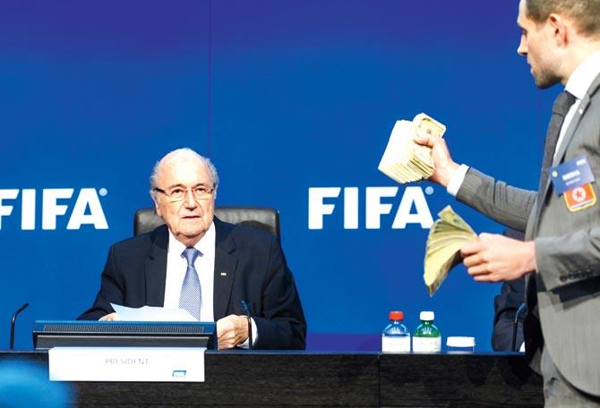 A British prankster Simon Brodkin (right) holds fake dollar notes as FIFA president Sepp Blatter prepares for a press conference in Zurich
