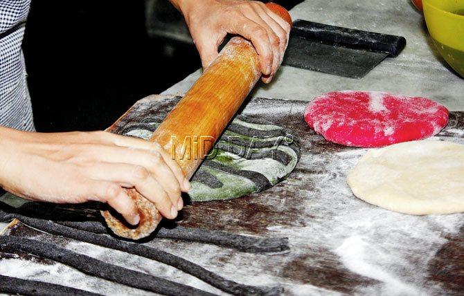 The black dough is cut into strips, placed on flattened green dough, and rolled into one form