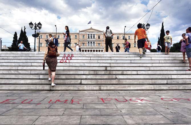 People walk past an anti EU (European Union) and anti IMF (International Monetary Fund) slogan in front of the Greek parliament in Athens, as Greece tries to avert a dangerous default that could spark a Greek Eurozone exit and raise serious questions about the future of the European Union