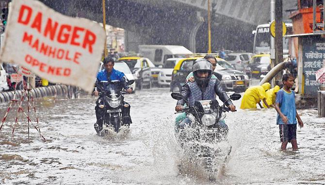 An open manhole sign is a familiar sight as vehicles wade through water logged roads. Pics/PTI
