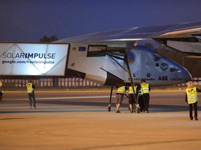 Support crew assist pilot Andre Borschberg (C) as he sits in the cockpit of Solar Impulse 2, the world