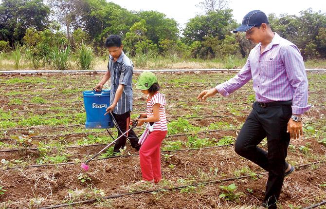 A worker shows a kid how to spray fertiliser on the crops