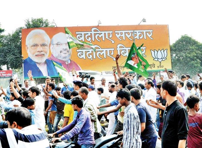 JD(U) supporters in Patna walk past a BJP hoarding as they celebrate the Mahagathbandhan’s victory in the Bihar Assembly polls on Sunday. Pic/PTI