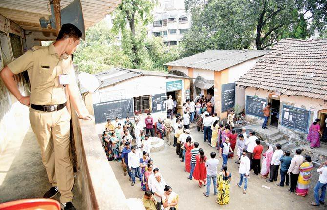 A policeman scans the polling booth at Sarangdhar School, Wadekar Road, Kalyan (West), from a vantage point. Long queues were witnessed at various polling stations throughout Kalyan-Dombivli yesterday. Pics/Sameer Markande