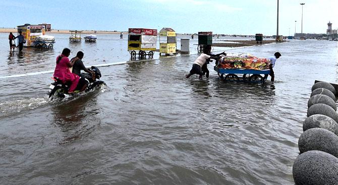 Vendors push a cart on the waterlogged Marina Beach in Chennai. PTI Photo