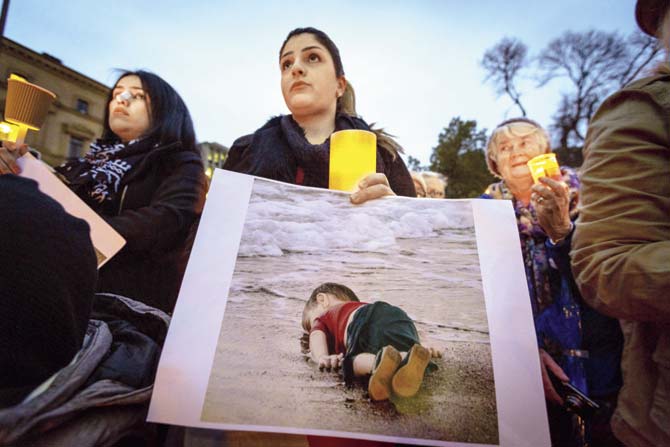 A woman in Melbourne, Australia in a candlelight vigil holds up a picture of Aylan Kurdi, the three-year-old who lost his life in an attempt to flee Syria. Pic/Getty Images