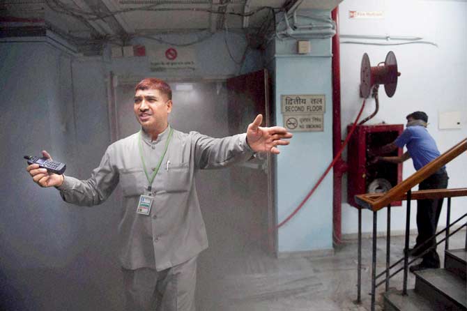 A security attendant asks people to vacate the building as smoke billows from the store section behind him. Pics/PTI