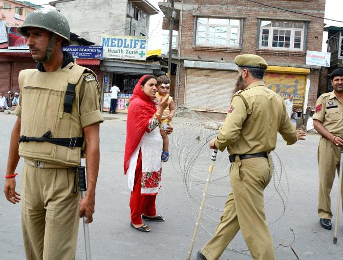 A Woman carrying her child seeks permission from a Police officer at a blocked road during the 34th day of curfew at Eidgah in Srinagar on Thursday.