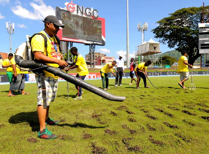 Ground staff use a blower to dry the field under the supervision of umpire Gregory Brathwaite (4L) during day 3 of the 4th and final Test between West Indies and India at Queen