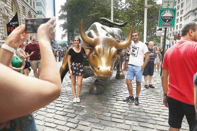 People take photos at the Wall Street Bull near the New York Stock Exchange (NYSE). Stocks fell after news that the US economy grew at the sluggish rate of 1.1 per cent. Despite the slowing growth rate Fed Chair Janet Yellen was optimistic about the economy. Pic/Getty Images/AFP