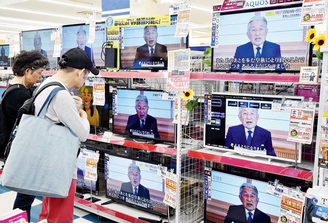 A couple looks at television screens showing a speech to the nation by Japanese Emperor Akihito. Pic/AFP	