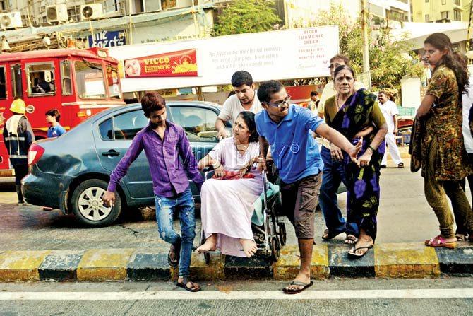 People helping an elderly wheel-chair-bound lady across the road after the building she stayed in caught fire. Pics/Bipin Kokate