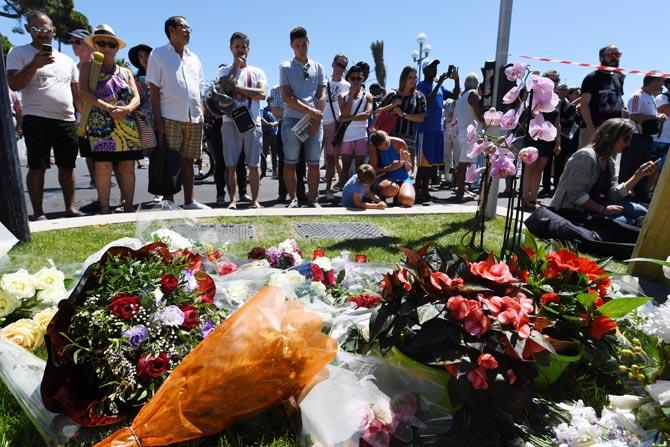 People stand in front of flowers and candles placed near the terror site in Nice. Pic/ AFP