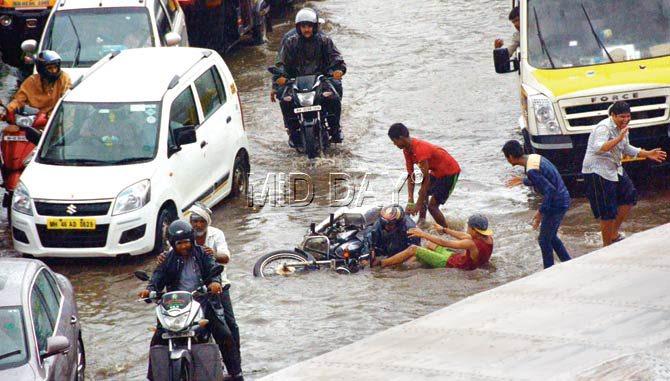 Passers-by rush to the aid of a motorcyclist, whose bike skid on a water-logged stretch on Santacruz Chembur Link Road on Saturday afternoon. Pic/Sayed Sameer Abedi