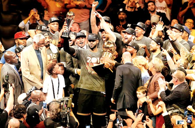 Cleveland Cavaliers star LeBron James centre holds his team-s Larry O’Brien NBA winners trophy and his own Finals MVP trophy after the 93-98 victory over Golden State Warriors in Game 7 of the NBA Finals in Oakland, California yesterday. The Cavs won the best-of-seven Finals 4-3