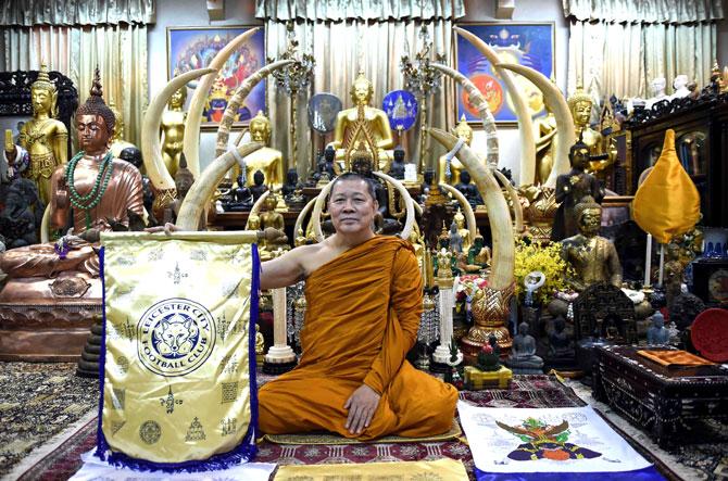 Thai Buddhist monk Phra Prommangkalachan holding a banner emblazoned with sacred patterns surrounding Leicester City Football Club