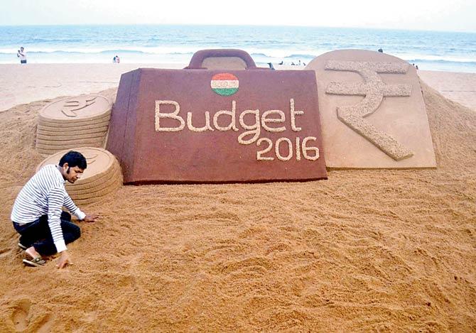 Sand artist Sudarsan Pattnaik makes a sand sculpture on upcoming Budget 2016 at Puri sea beach of Odisha on Sunday. Pic/PTI