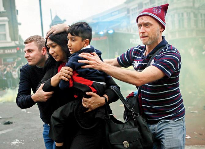 A woman and a child are helped past West Ham fans as people become violent at police outside the Boleyn ground. Pic/Getty Images