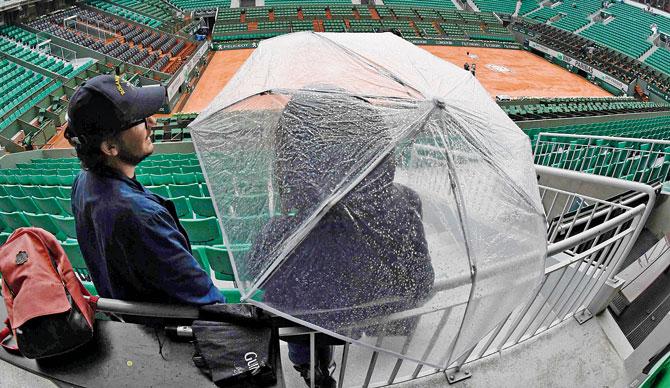 Spectators stand with an umbrella after play is suspended due to rain at the French Open in Paris yesterday. Pic/AFP
