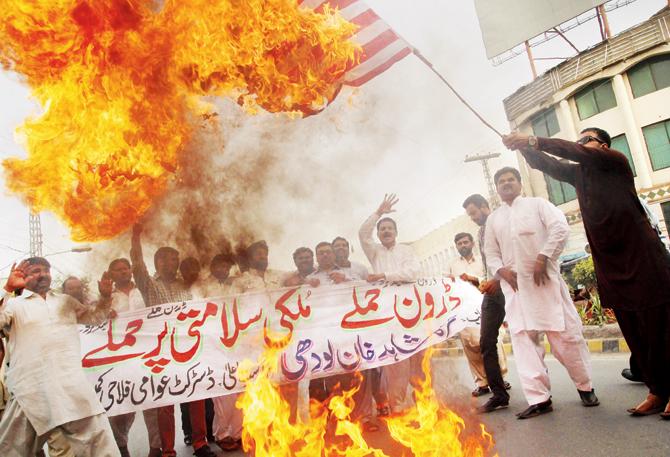 A Pakistani demonstrator holds a burning US flag as others shout slogans during a protest in Multan against the drone strike. Pic/AFP