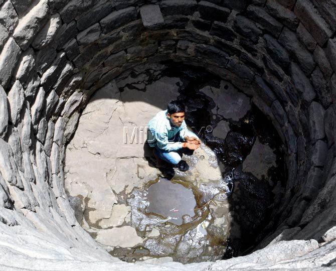 A villager tries to scoop whatever little water he can from one of the two wells in Owe Camp village in Kharghar
