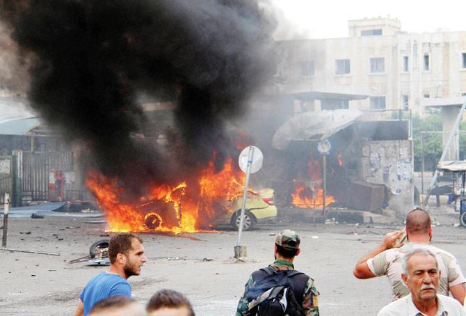 People gather around a burning car  at a spot where suicide bombers  blew themselves up, in Tartus. Pic/AP