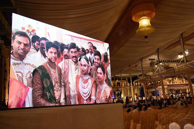 Indian mining tycoon, Gali Janardhan Reddy, (C) is seen on a big screen as he poses with his daughter Bramhani (2R) and son-in-law, Rajeev Reddy (2L) during their wedding at the Bangalore Palace Grounds in Bangalore. AFP PHOTO / STRINGER