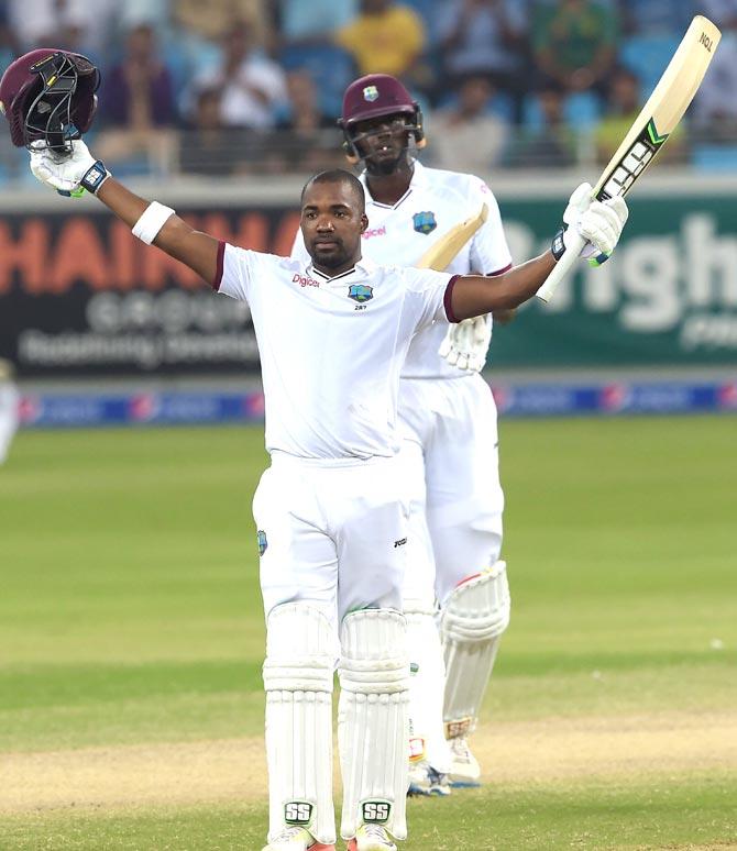 West Indies batsman Darren Bravo (front) raises his bat and helmet as he celebrates after scoring century (100 runs) as team captain Jason Holder looks on on the final day of the first day-night Test. Pic/AFP