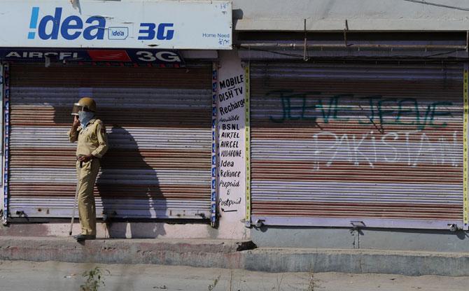 An Indian policeman speaks on a mobile phone in front of closed shops during clashes between Indian government forces and kashmiri protestors in Srinagar. Pic/ AFP