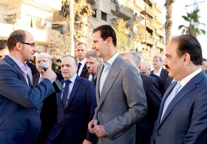 Syrian President Bashar al-Assad (C) speaking with the press as he walks in the street alongside officials after performing the morning Eid al-Adha prayer at a mosque in a government-controlled area of Daraya