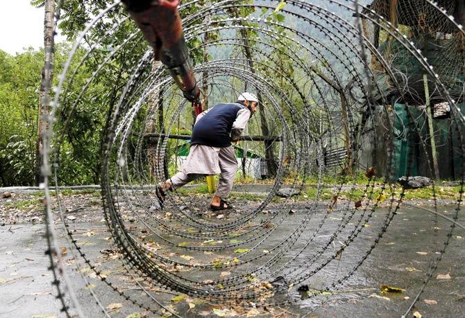 A Kashmiri man ducks to cross an iron barricade with coils of razor wire near a military base at Braripora, near the LoC. Pic/AP