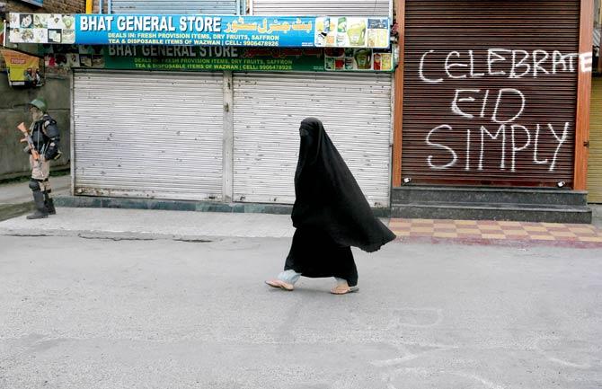 A veiled Kashmiri woman walks past graffiti on a closed shop in a deserted market in Srinagar on Sunday. Pic/AP