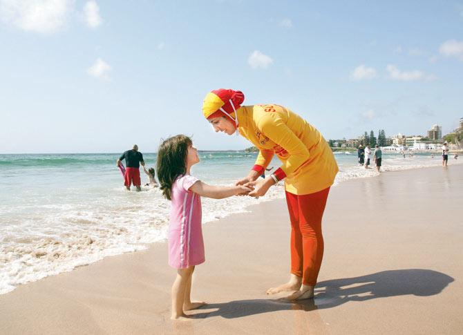 An Australian lifequard talks to a young girl whilst wearing a burkini on her first surf lifesaving patrol at North Cronulla Beach in Sydney. The red and yellow ‘burkini’ was specially designed for Muslim lifesavers to allow females to fulfil both their patrolling and religious obligations.  Pic/Getty Images