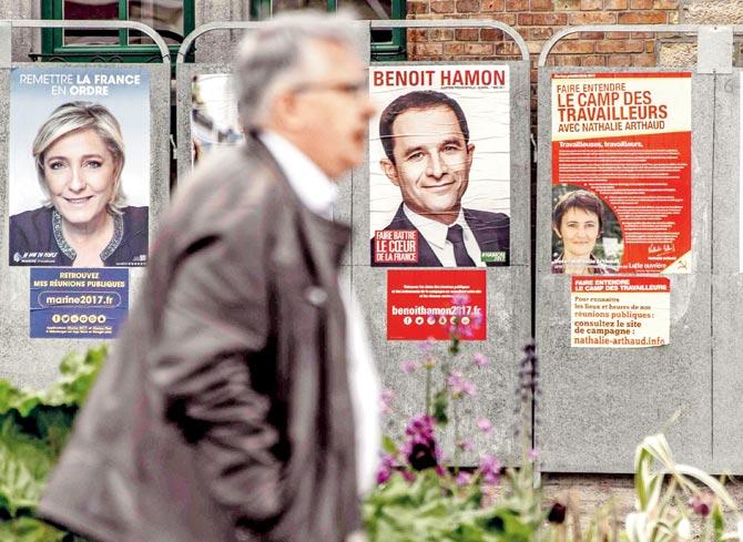 Man walking past campaign posters of French presidential election candidates in Bailleul