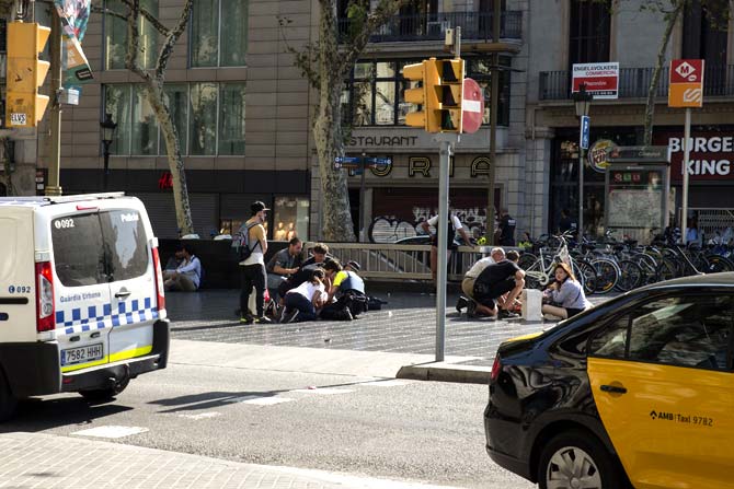People help injured persons after a van ploughed into the crowd, killing at least 13 people and injuring around 100 others on the Rambla in Barcelona. Pic/AFP