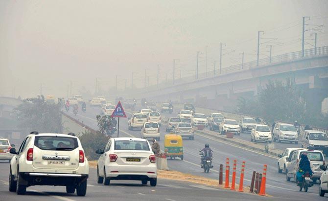Vehicles make their way through the morning smog at New Delhi. Pic/PTI